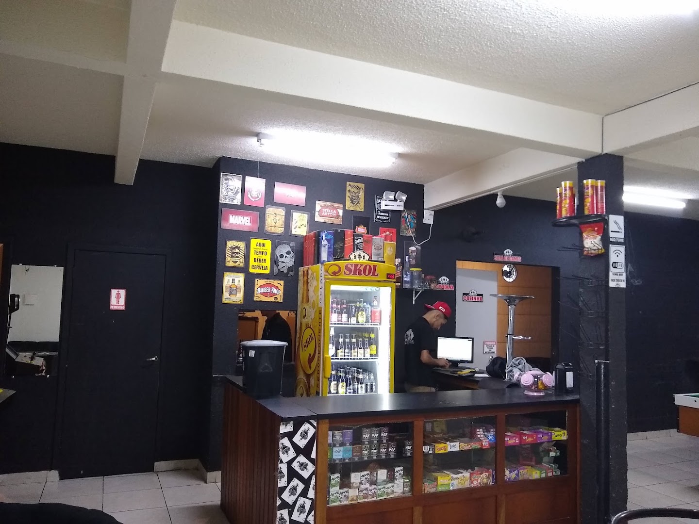 Balcão com geladeira de bebidas e sala de jogos dentro da Barbearia Az De Espadas